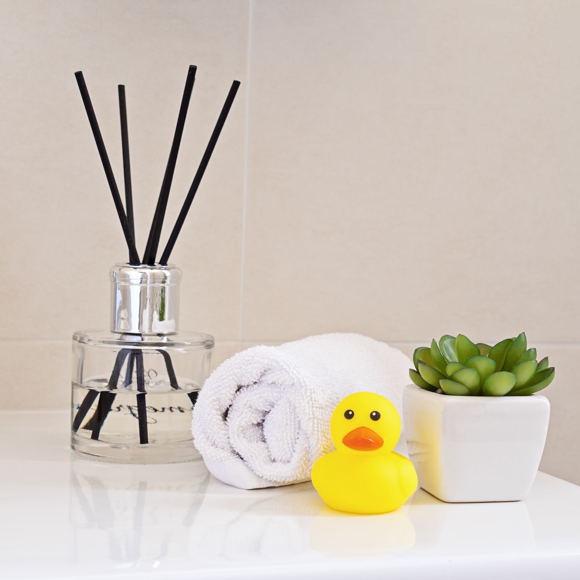 Air fragrant perfumed on sink in the bathroom with white wrapped towel and yellow rubber duck. Chrome water tap and sink. Bathroom interior and accessories concept, square format