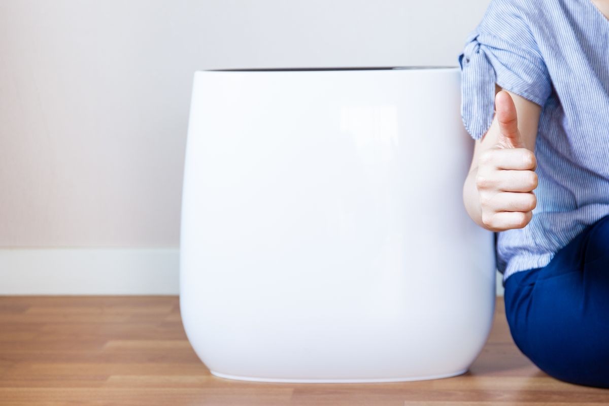 Woman showing a thumb up beside the modern air purification machine close up.