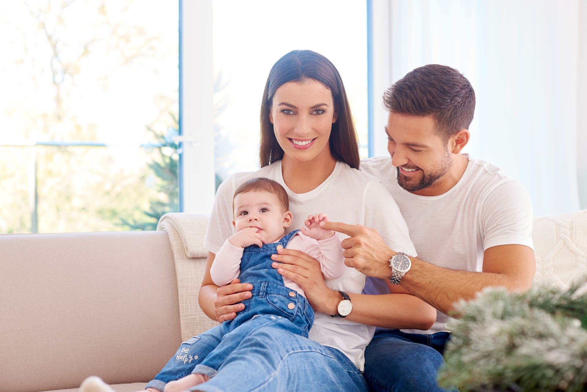 Shot of happy young family sitting on sofa with their baby girl and enjoy relaxing at home. 