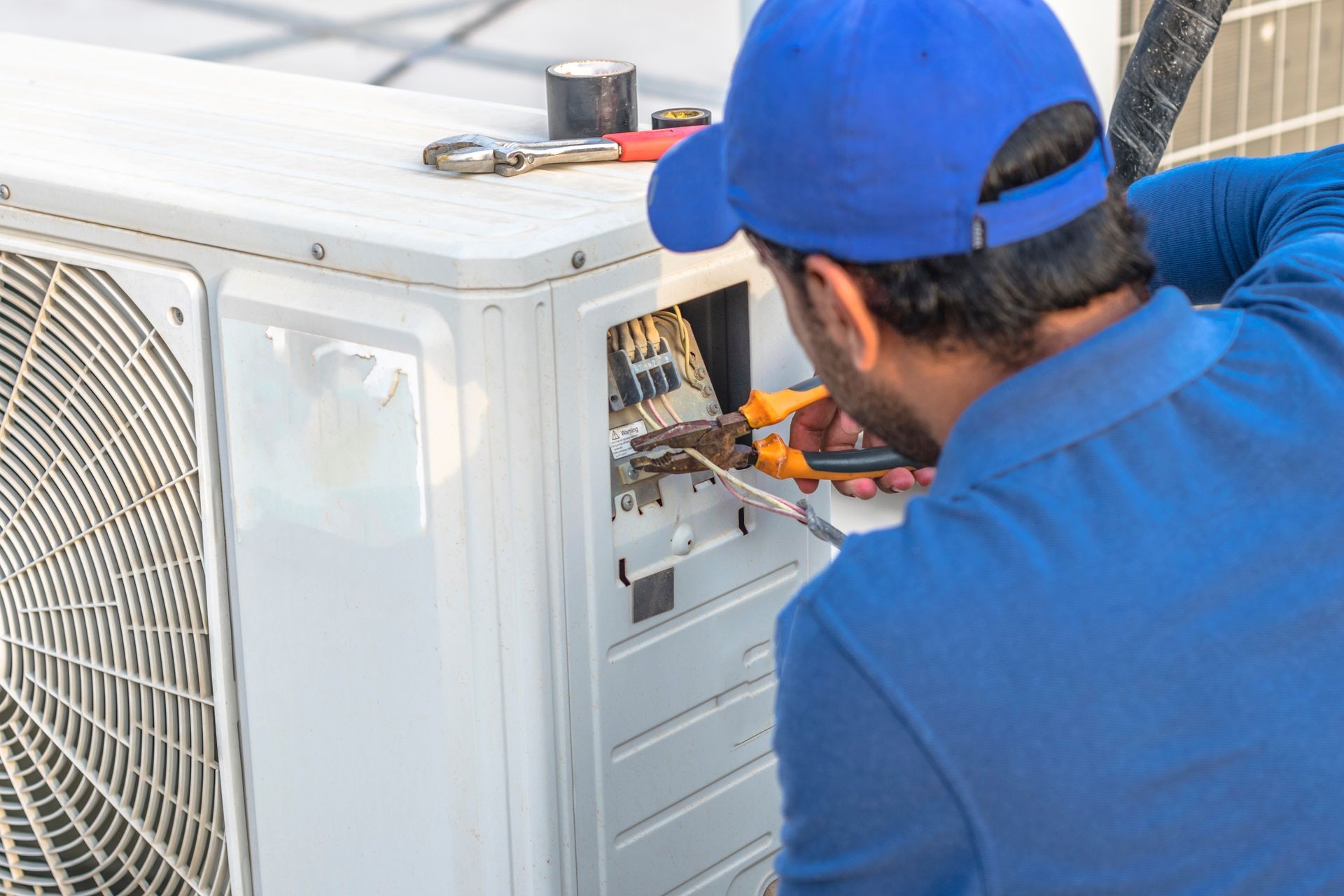 a professional electrician man is fixing the heavy air conditioner by his tools on the roof top and wearing blue color of uniform and head cap