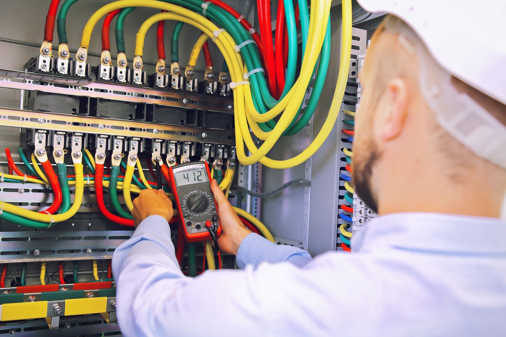 Electrician engineer measures voltage with multimeter in high voltage cabinet.